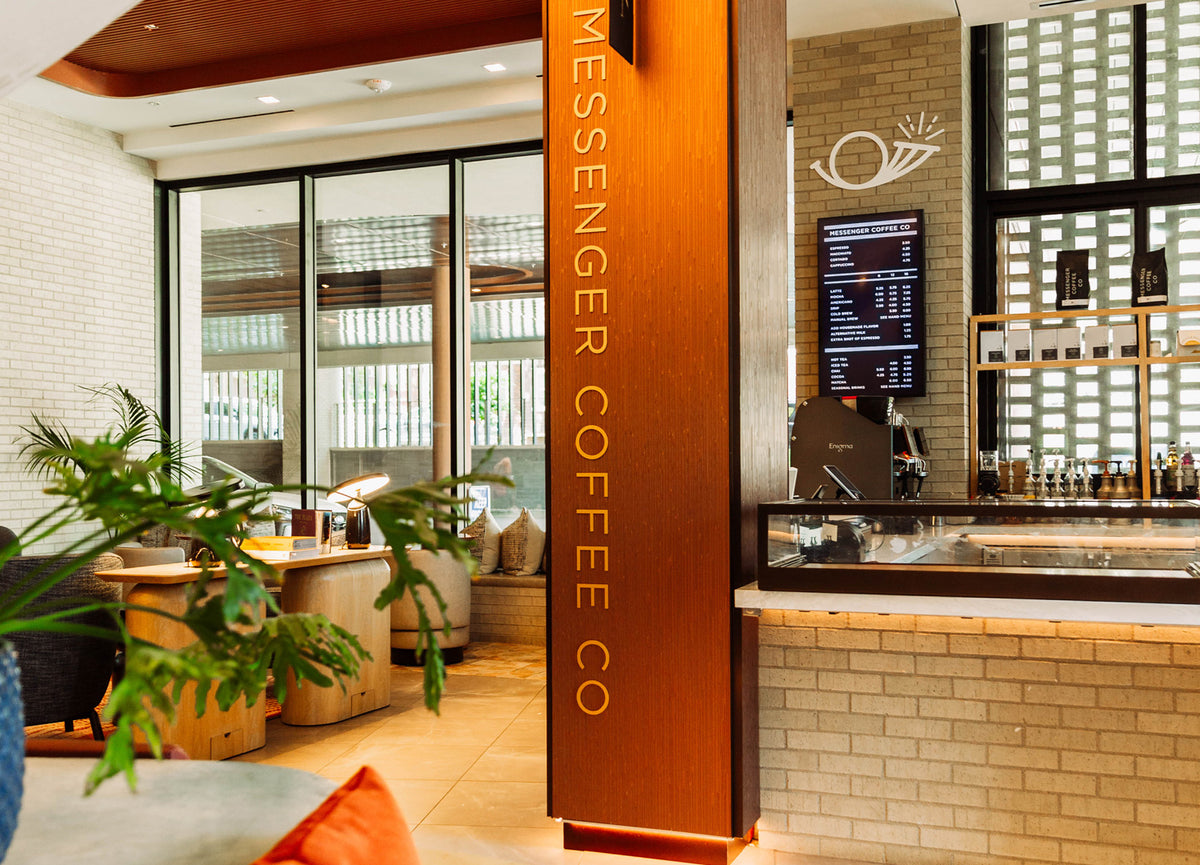 Modern coffee shop interior with seating area, wooden pillar, menu screen, and brick walls in warm lighting